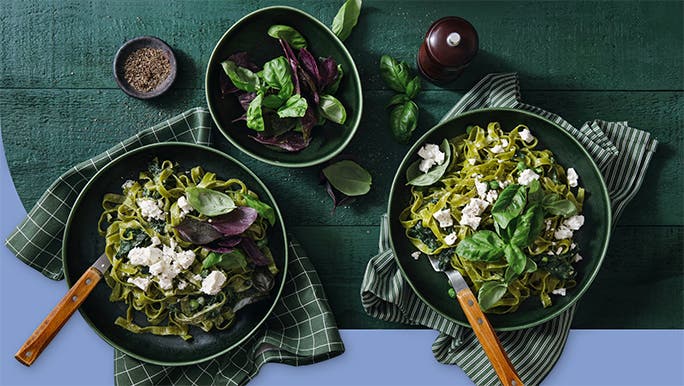 Two bowls of spinach and feta pasta with a green side salad
